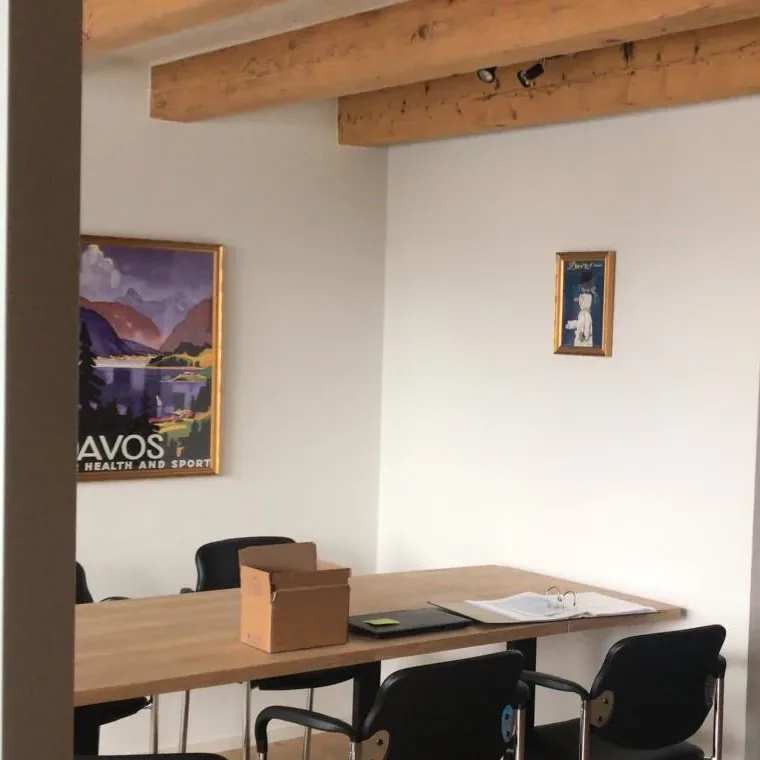 An apartment room set up as an office, with a long table, black conference chairs, files and a vintage Davos poster on the wall