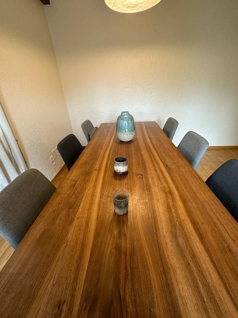 A long wooden dining table with upholstered chairs in a Davos apartment, used as a team meeting room