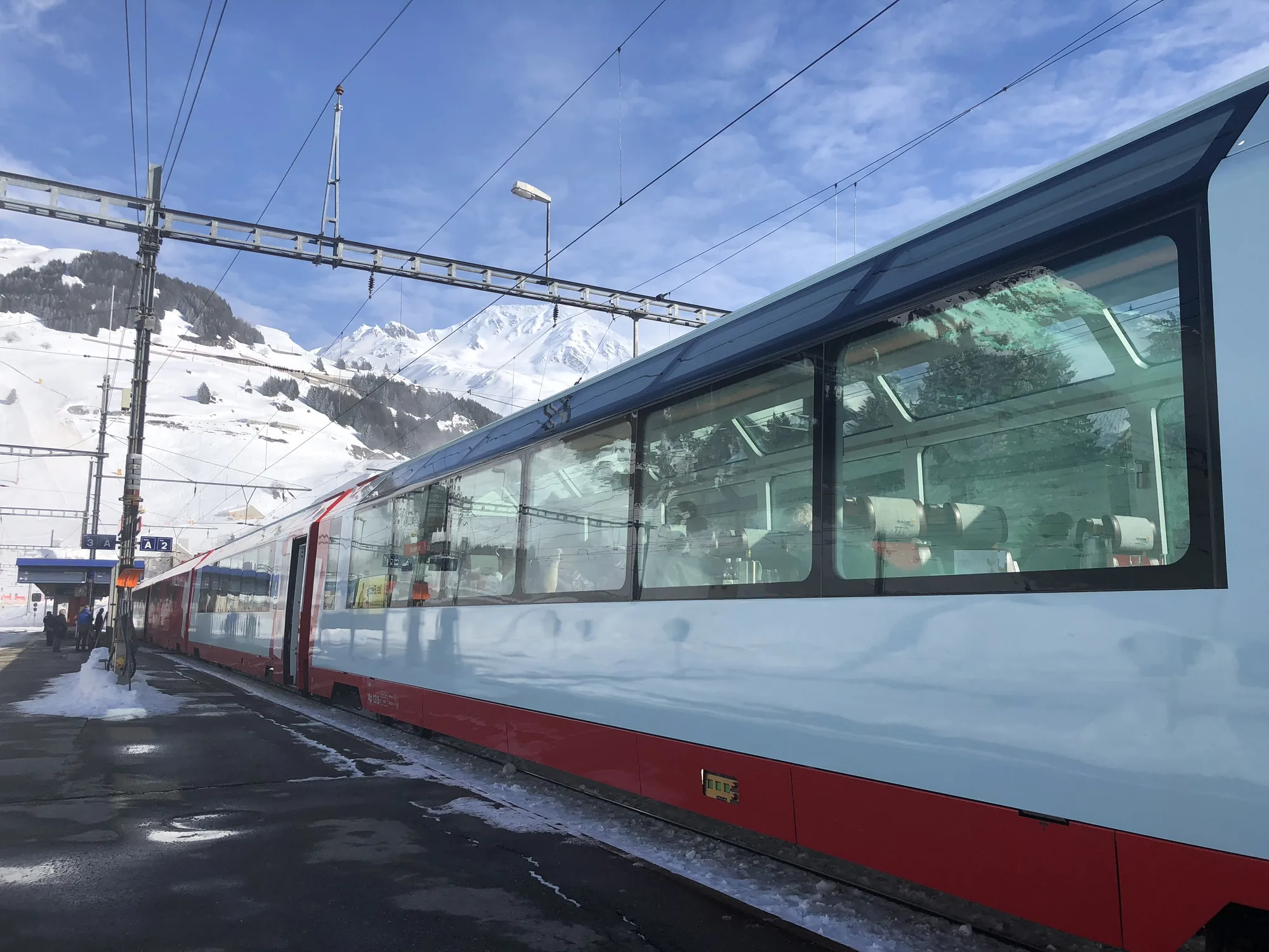 A Rhaetian Railway train stopped at a snowy mountain station, peaks in the background